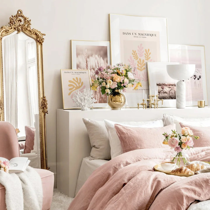 Decorative bedroom with pink bedding, floral arrangements, and framed artwork. 