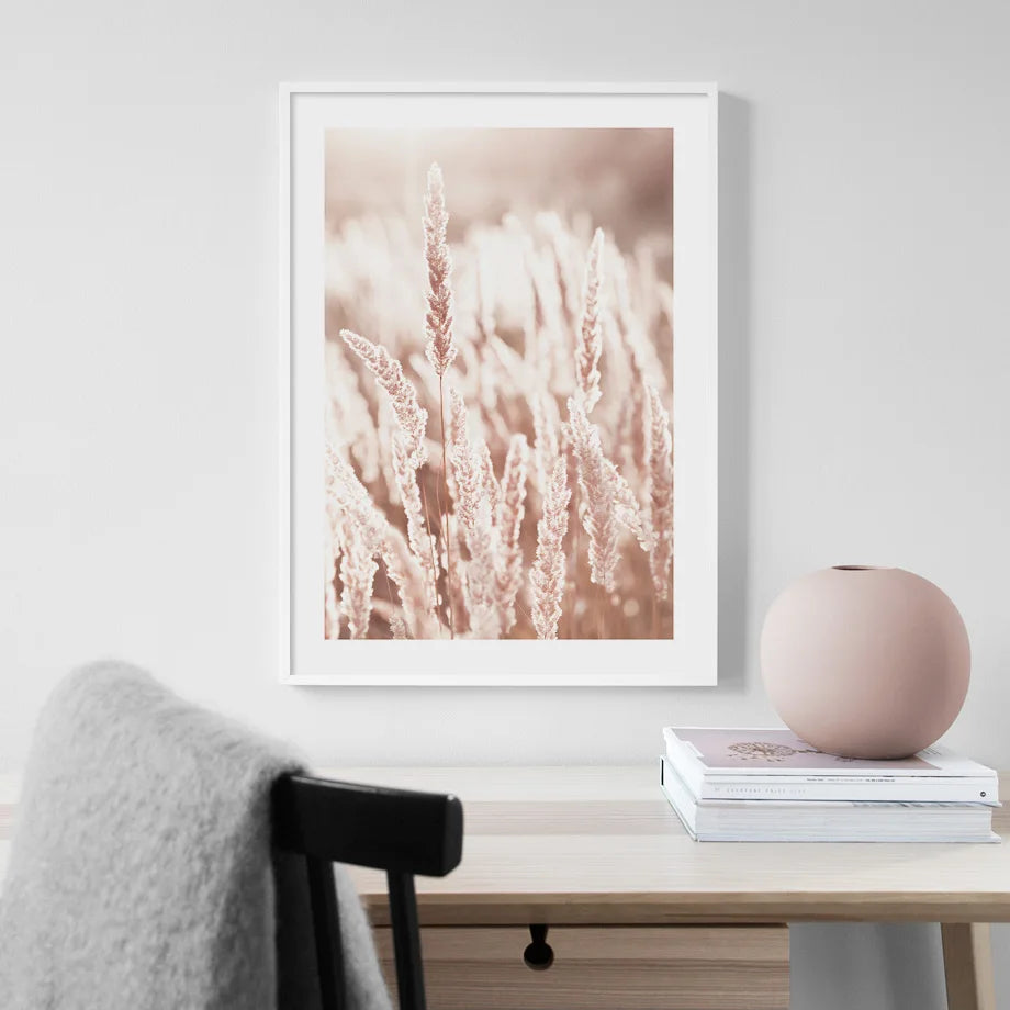 Framed artwork of floral design on a wall above a table with books and a vase.