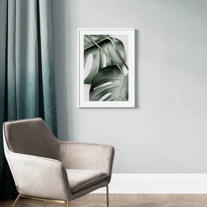 Framed artwork of green leaves on a wall above a modern chair.